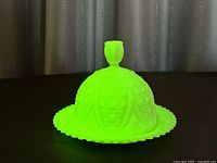 Photo under UV light showing bright green uranium Vaseline satin glass dish with lid in place, emphasizing glow effect.