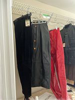 Three pieces hanging on rack: black suede leather pants, black midi pencil leather skirt with buttons, and red leather pants.