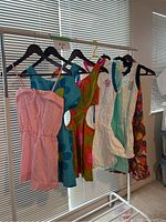 Seven garments hanging on white rack in front of blinds
