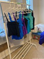Eight silky summer tank tops hanging on a white garment rack in assorted colors including black, blue, purple, and teal.