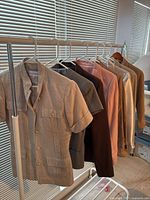 Eight women's blazers hanging on a rack by a window, showing different colors and styles.