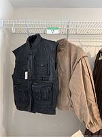 Photo showing black leather vest with multiple pockets and tan bomber jacket hanging side by side on a rail