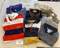 Eight men's rugby and polo style shirts laid out on a white background. Various colors including red, white, navy, purple, beige, and brown, different plaid and stripe patterns. Mix of Adidas, Point Zero, and Wimbledon brands.