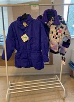 Two Eddie Bauer snow jackets on hangers displayed on a white rack by a window, showing front and side of jackets.