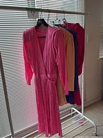 Full view of four garments on hangers including a vibrant pink long wrap dress and three silky skirt sets in orange, purple with polka dots, and dark pink.