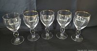 Five crystal Irish coffee glasses with gold rims and shamrock design on flattened stems, arranged side by side.