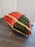 Ethiopian sun umbrella folded partially, showing red and green panels with gold decorative pattern and gold fringe trim, wooden handle visible