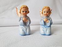 Two porcelain Goebel angels side by side, showcasing detailed hand-painting on robes, wings, and faces.