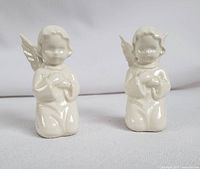 Two white vintage Goebel angels kneeling with hands folded, shown from front view.