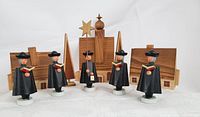 Full group shot of five wooden caroller figures standing in front of wooden church, two houses, and two trees.
