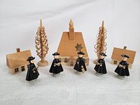 All items arranged: church in the center, two houses on each side, two curly wooden trees behind, five black-robed carollers in front.