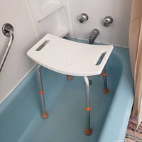 Front view of the shower stool placed inside a blue bathtub showing the seat with handle slots and adjustable legs with rubber feet.