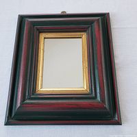 Front view of the wall mirror showing dark red and black wooden frame with gold inner trim surrounding the mirror glass.
