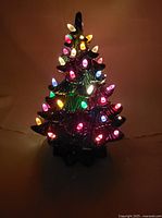 Vintage ceramic Christmas tree lamp illuminated in the dark showing multicolored bulbs glowing.