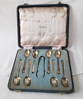 Set of 8 vintage sterling silver English teaspoons and small sterling silver tong in original blue presentation case with pink satin lining.