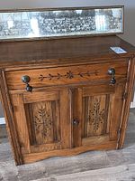 Front view of the antique wooden wash stand cabinet showing detailed floral carvings on drawer and door panels, metal handles, and smooth top surface.