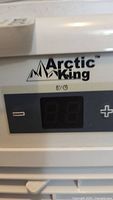 Close-up of Arctic King logo on the air conditioner's digital control panel with temperature adjustment buttons.