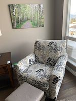 Armchair angled view showing upholstery pattern and size relative to side table and window