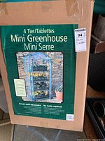 Box packaging of the 4 tier mini greenhouse with clear cover and metal frame shown on front.