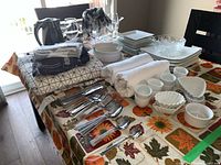Overview of dinnerware, glassware, cutlery, table linens, and kettle on table with autumn-themed cloth