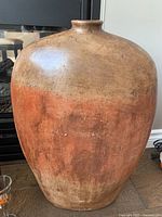 Large burnt orange and tan pottery vase with narrow neck, showing color and texture.