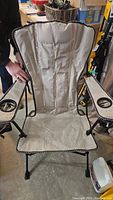 Front view of a beige folding camping chair with padded back, black metal frame, and armrests with mesh cup holder