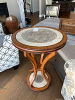 Full view of the circular curvy warm wood side table placed between furniture, showing the decorative mosaic tile inset on top and base.