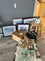 Overview showing quilt, wooden stool, wooden storage box, framed pictures, floral pillow, and wrapped hangers.