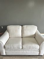 Front view of the off-white linen look love seat showing two seat and two back cushions with armrests and a low profile.