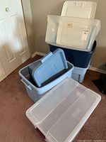 Six assorted plastic storage bins stacked and arranged on carpeted floor in a room.