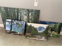 Four canvas nature prints displayed leaning against a wall, showing forest, lake, and mountain themes.