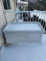 Front view of Rubbermaid outdoor storage bench covered lightly with snow, positioned on balcony.