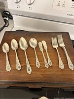 Eight silverplate utensils displayed atop wooden flatware box