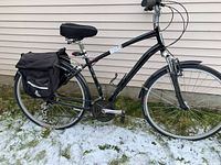 Full side view of black Specialized bicycle with pannier bag and tires flat, pictured outside on grass with some snow.