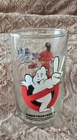 Front view of the clear drinking glass showing the Ghostbusters ghost logo holding up two fingers and characters in action.
