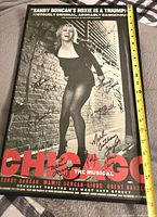 Full view black-and-white Chicago The Musical poster featuring a woman in costume with multiple cast signatures on the poster, showing size reference with ruler.