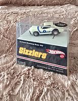 Front angle view of the Hot Wheels Sizzlers '70 Ford Mustang Boss 302 die cast car in original sealed packaging on a textured surface.