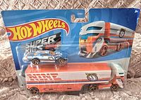 Photo of new, sealed Hot Wheels Super Rigs featuring a large toy rig truck and a smaller race car on top in original packaging.
