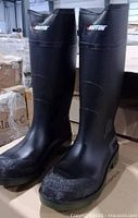 Front and side view of the pair of BAFFIN black rubber boots with reinforced toe area and brand logos.