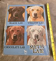 Front photo of the new tin sign showing four Labrador dog illustrations labeled Black Lab, Yellow Lab, Chocolate Lab, and Meth Lab.