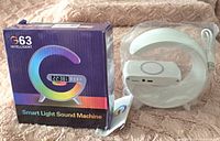 Photo showing the product box labeled 'G63 Intelligent Smart Light Sound Machine' with the crescent-shaped white device and manual beside it.