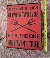 Front of rectangular red tin sign with the quote and crossed pitchfork graphic, a measuring tape shows approximately 12 inches wide.