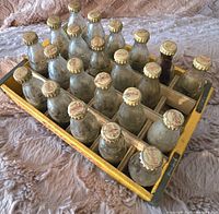 Top-down view of the yellow wooden Coca-Cola crate with 22 miniature glass bottles, two slots empty, showing metal capped bottles.
