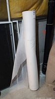 Photo of an upright white bolt of fabric with some fabric unrolled, placed against a yellow insulation wall and near other basement items.