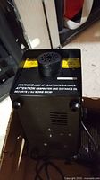 Photo showing top and front of first black fog machine with safety warning label and vent