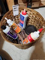 Basket containing multiple adhesive bottles, small paint can, sandpaper, and box cutter