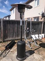Full view of outdoor propane heater showing complete height with black cylindrical base and round metal top reflector.