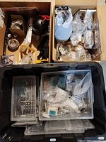 Wide view of two boxes and plastic container holding multiple small parts like knobs, circuit boards, furniture feet, and miscellaneous items.