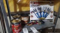 Shelf display showing Minwax Pre-Stain can, Saman One Step Wood Stain can, sealed ProPainter paint brushes set with blue handles, used paint brushes, and price tags.
