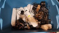 Blue bin containing multiple power adapters, power supplies, and cords, tangled together with some wrapped in bubble wrap.